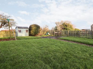 A grassy backyard with a swing set shed slide and a table with chairs at Garden Cottage in Chathill near Beadnell