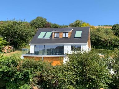 A house with large windows and solar panels on the roof surrounded by trees and greenery at Beach View in Combe Martin