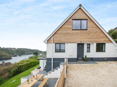 A house with wooden paneling and gravel driveway near a coastline with trees and water at Beach View in Combe Martin