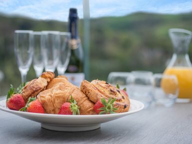 A plate with croissants, pastries, and strawberries on a table with glasses, a bottle, and a jug of orange juice in the background at Beach View in Combe Martin