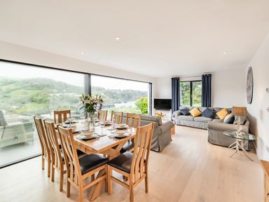 A dining table with eight chairs set with plates and glasses in a living room with sofas and a large window at Beach View in Combe Martin