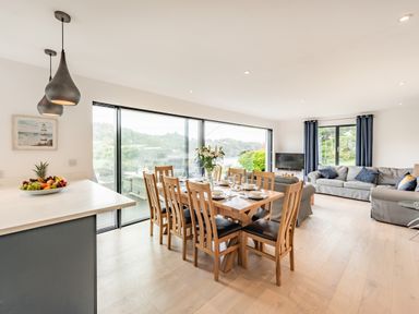 A dining area with wooden table and chairs adjacent to a living room with sofas and a television at Beach View in Combe Martin