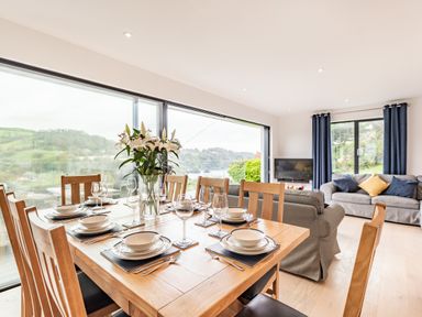 A dining table set with plates and glasses next to a sitting area with sofas and a television at Beach View in Combe Martin