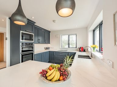 A kitchen with blue cabinets and a marble countertop with fruit bowl and pendant lights at Beach View in Combe Martin