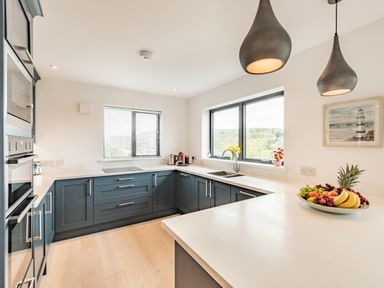 A kitchen with blue cabinets white countertops pendant lights and fruit bowl at Beach View in Combe Martin