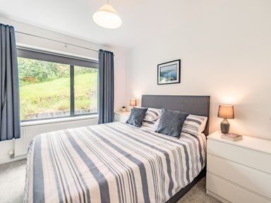 A bedroom with a bed striped bedding lamps and a large window at Beach View in Combe Martin