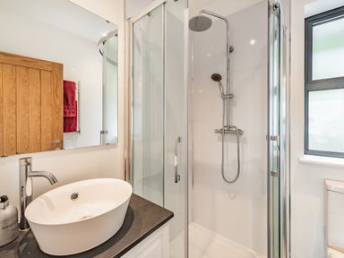 A bathroom with a white sink on a black countertop a glass shower with chrome fixtures and a window at Beach View in Combe Martin