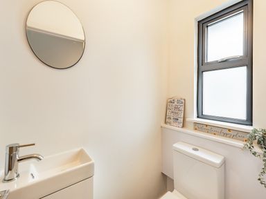 A small bathroom with a white sink and toilet a round mirror and a window with decorative signs on the sill at Beach View in Combe Martin