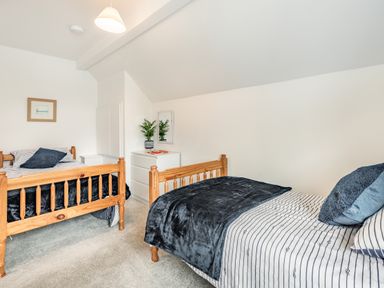 A bedroom with two wooden single beds white dresser with a plant and mirror at Beach View in Combe Martin