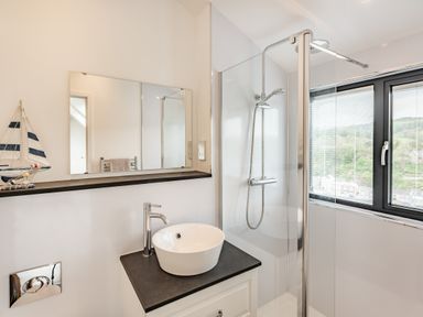 A bathroom with a countertop basin sink mirror shower area and window at Beach View in Combe Martin
