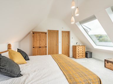 A bedroom with a bed with pillows and a blanket a wooden wardrobe wooden chest of drawers two wooden doors and a large skylight window at Beach View in Combe Martin
