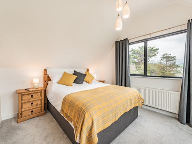 A bedroom with a bed yellow and gray pillows wooden bedside tables lamps and a window with gray curtains at Beach View in Combe Martin