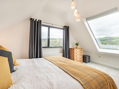 A bedroom with a bed and pillows next to windows with curtains and a chest of drawers with a plant at Beach View in Combe Martin