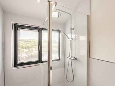 A shower area with a glass door and a window showing a hillside view at Beach View in Combe Martin