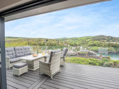 An outdoor patio with wicker chairs and a table overlooking hills and water at Beach View in Combe Martin