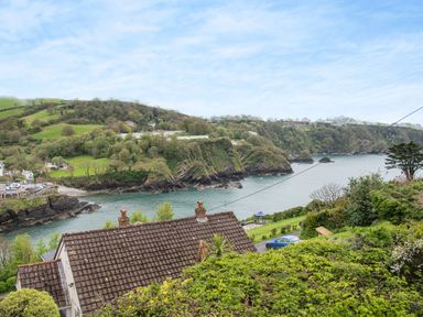 A coastal view with a tiled roof house trees a blue car and a rocky shoreline at Beach View in Combe Martin