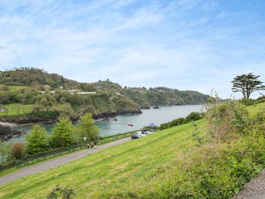 A coastal scene with a grassy hill path trees a gazebo and rocky cliffs by the sea at Beach View Combe Martin