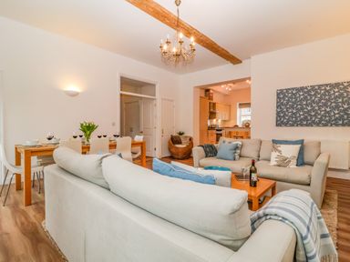 A living room with sofas dining table set with wine glasses and a kitchen in the background at Feathers Blythburgh in Reydon