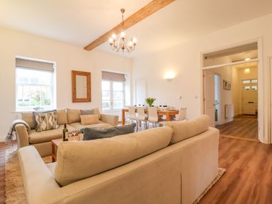 A living room with two beige sofas a wooden dining table with white chairs and a chandelier at Feathers Blythburgh in Reydon