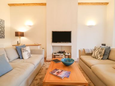 A living room with two sofas a wooden coffee table and a wall-mounted television at Feathers Blythburgh in Reydon