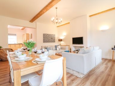 A dining table set with bowls and wine glasses next to a sitting area with sofas and a wall-mounted TV at Feathers Blythburgh in Reydon