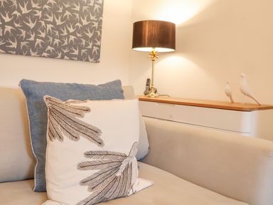 A beige sofa with two cushions next to a white cabinet with a lamp phone and bird decorations at Feathers Blythburgh in Reydon