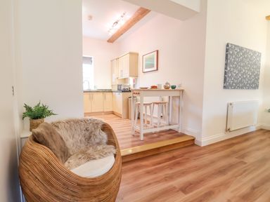 A kitchen and seating area with wooden flooring a high table with stools and a wicker chair with cushions at Feathers Blythburgh in Reydon