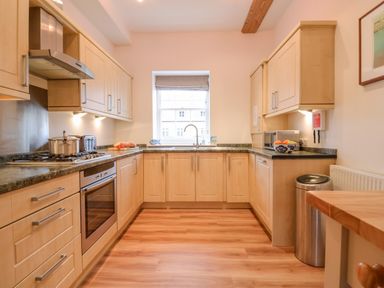 A kitchen with wooden cabinets green countertops a stove oven a window and a trash can at Feathers Blythburgh in Reydon