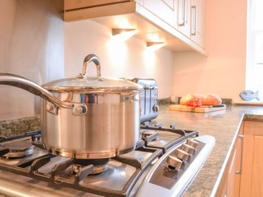 A kitchen with a stainless steel pot on a gas stove a toaster on the counter and bread with tomatoes on a cutting board at Feathers Blythburgh in Reydon