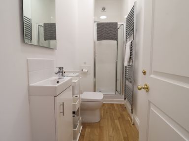 A narrow bathroom with a sink cabinet toilet shower and heated towel rack at Feathers  Blythburgh in Reydon
