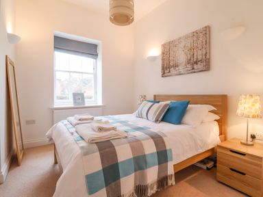A bedroom with a double bed with folded towels bedside tables and a window at Feathers Blythburgh in Reydon