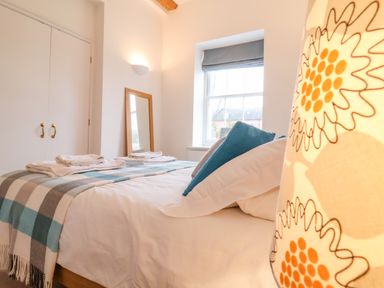 A bedroom with a bed covered in white and blue linens and a standing mirror near a window at Feathers Blythburgh in Reydon