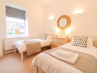 A bedroom with two single beds a wooden dresser and a round mirror above it at Feathers Blythburgh in Reydon
