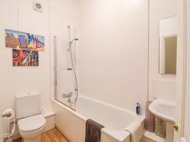 A bathroom with a toilet a bathtub with shower a sink and wall art at Feathers Blythburgh in Reydon