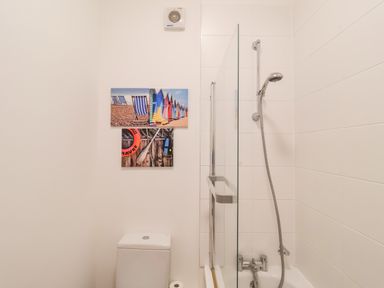 A bathroom with a toilet and a bathtub with a shower and three beach-themed pictures on the wall at Feathers Blythburgh in Reydon
