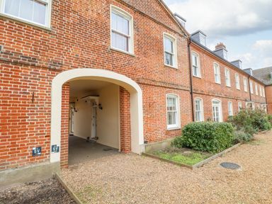 A brick building with white framed windows a large archway and bushes along a gravel path at Feathers  Blythburgh in Reydon