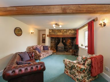 A living room with floral and leather sofas a stone fireplace and a wood stove at Canny Croft in Chilton Polden near Street