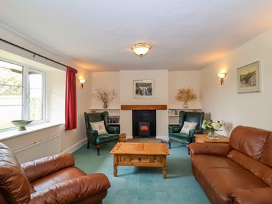 A living room with two brown leather sofas two green armchairs a wooden coffee table and a fireplace at Canny Croft in Chilton Polden near Street