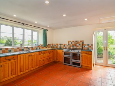 A kitchen with wooden cabinets a double oven tiled backsplash and terracotta floor at Canny Croft in Chilton Polden near Street