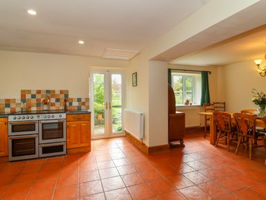 A kitchen with a stove and wooden cabinets next to glass doors leading outside and a dining area with wooden table and chairs at Canny Croft in Chilton Polden near Street