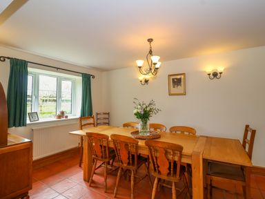 A dining room with a wooden table and chairs a window with green curtains and wall lights at Canny Croft in Chilton Polden near Street