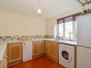 A kitchen with wooden cabinets a washing machine a refrigerator a sink under a window and tiled floor at Canny Croft in Chilton Polden near Street