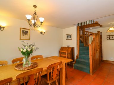 A dining room with wooden table and chairs next to a staircase with green carpet at Canny Croft in Chilton Polden near Street