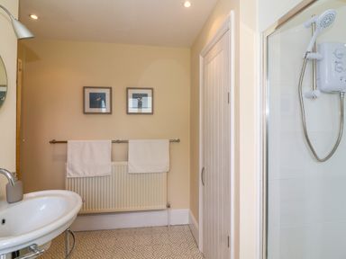 A bathroom with a sink a shower a door two framed pictures two towels on a rail and a radiator at Canny Croft in Chilton Polden near Street