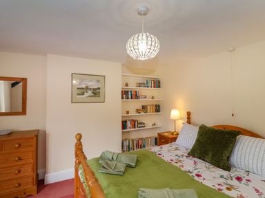 A bedroom with a wooden bed dressed with green and floral bedding a wooden chest of drawers and shelves with books at Canny Croft in Chilton Polden near Street
