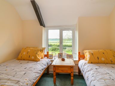 A bedroom with two single beds separated by a wooden table under a window at Canny Croft in Chilton Polden near Street