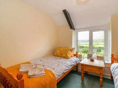 A bedroom with two single beds a wooden side table and a window showing a garden and fields at Canny Croft in Chilton Polden near Street