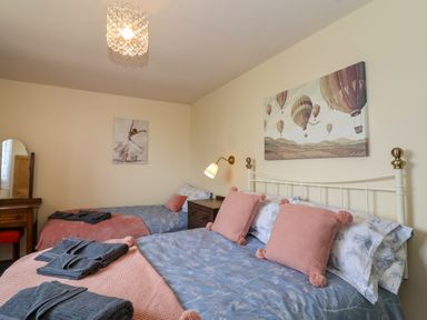 A bedroom with two beds dressed in blue and pink bedding with pillows towels and paintings on the walls at Canny Croft Chilton Polden near Street