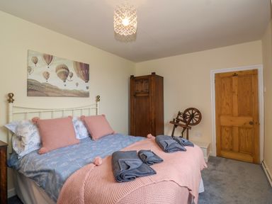 A bedroom with a bed with pink pillows and blankets blue bedsheets a wooden wardrobe and a spinning wheel at Canny Croft in Chilton Polden near Street