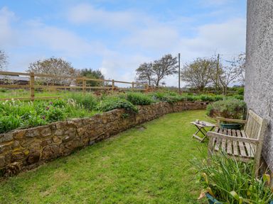 A garden area with a wooden bench and small table beside a stone wall and grass at Canny Croft Chilton Polden near Street